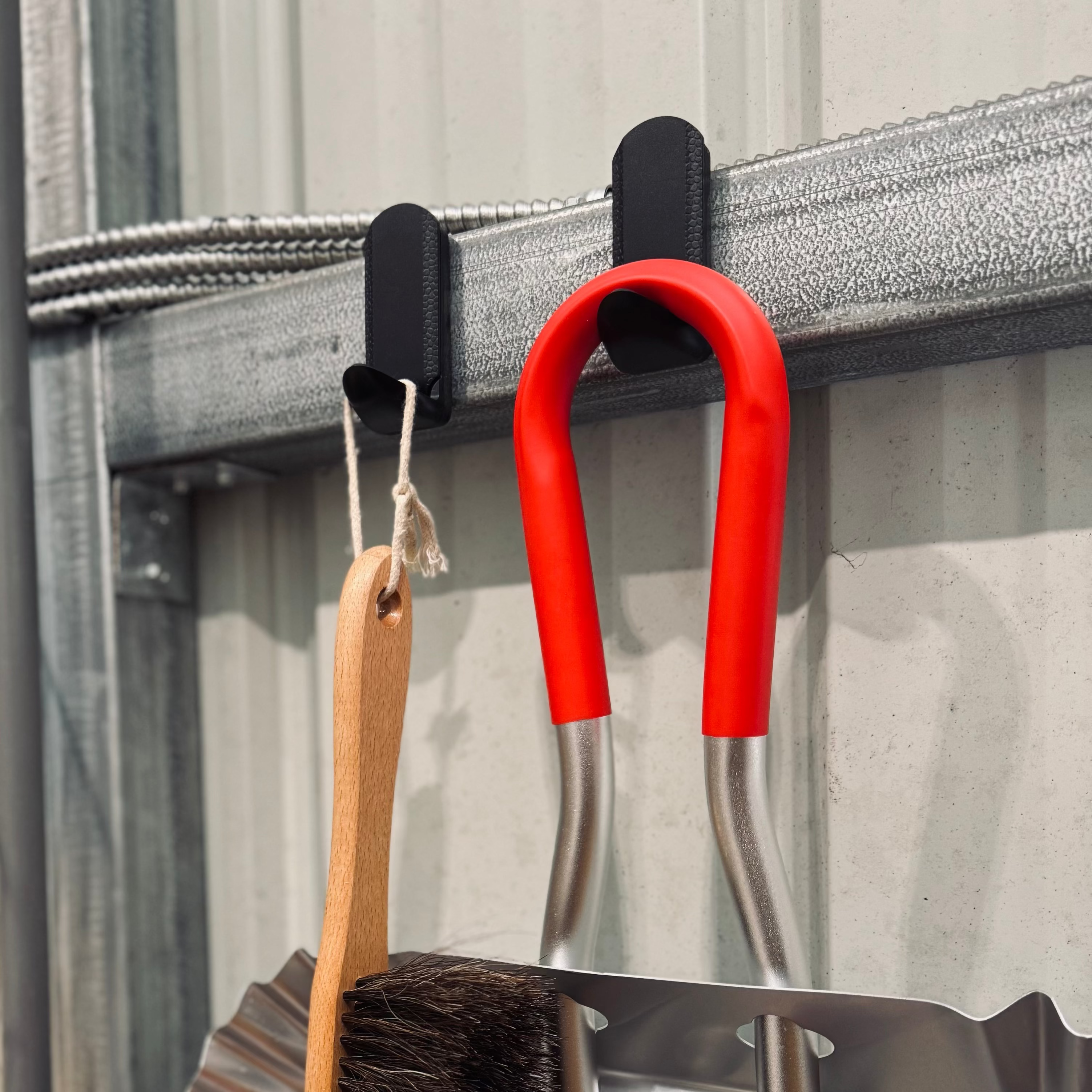 Two red Gator Magnetics magnetic hooks hang on a corrugated steel wall panel in a pole barn, supporting a paintbrush with a wooden handle and a tool with red-covered handles, showcasing efficient garage wall storage systems.