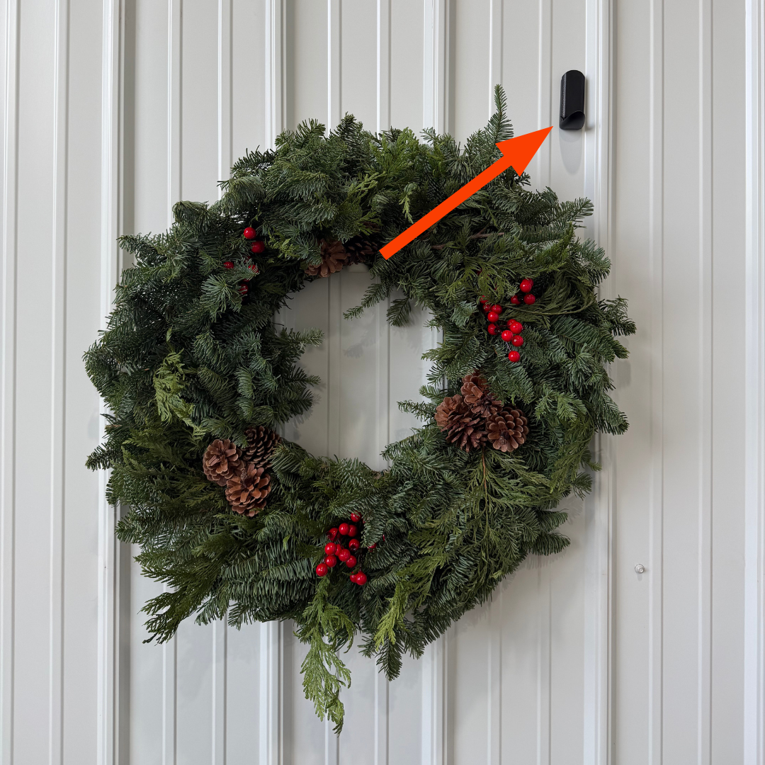 A holiday wreath is hung on a white steel pole barn wall using a black Gator Magnetics magnetic hook, demonstrating an effortless and secure way to store seasonal items.