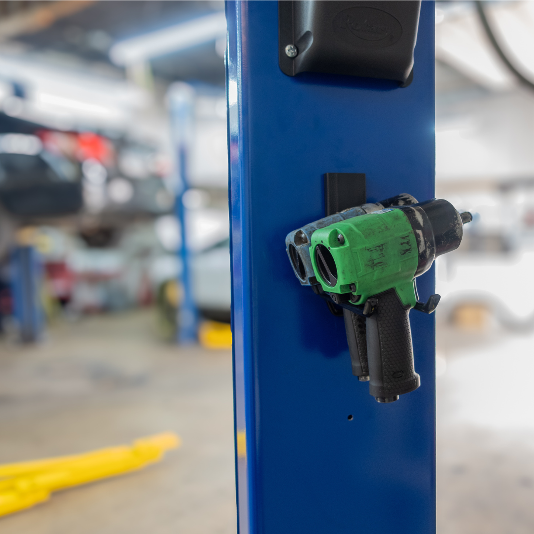Two impact wrenches are securely hung on a blue steel lift post in a busy automotive workshop using Gator Magnetics magnetic locker hooks, showcasing tool organization on a steel surface without drilling or permanent installation.