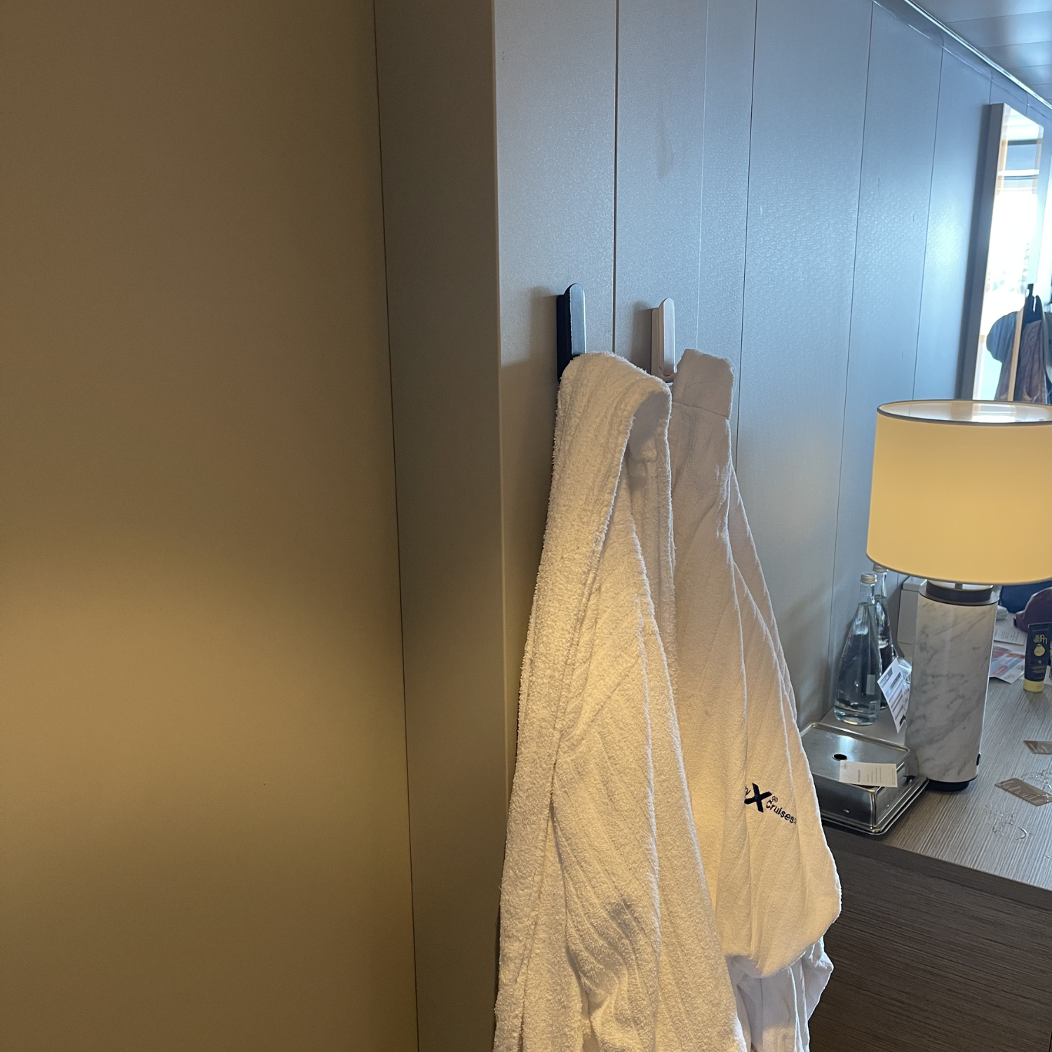 Two white robes hang on red and gray Gator Magnetics magnetic hooks attached to a smooth, flat steel wall panel in a room setting with a lamp and tabletop items visible nearby.