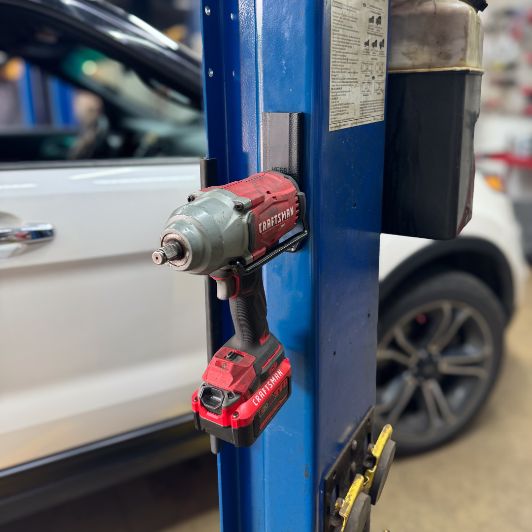 A red and gray Craftsman cordless impact driver is securely held on a blue steel post using a black Gator Magnetics hook, demonstrating a clean, tool-free storage solution for power tools in a professional garage setting.