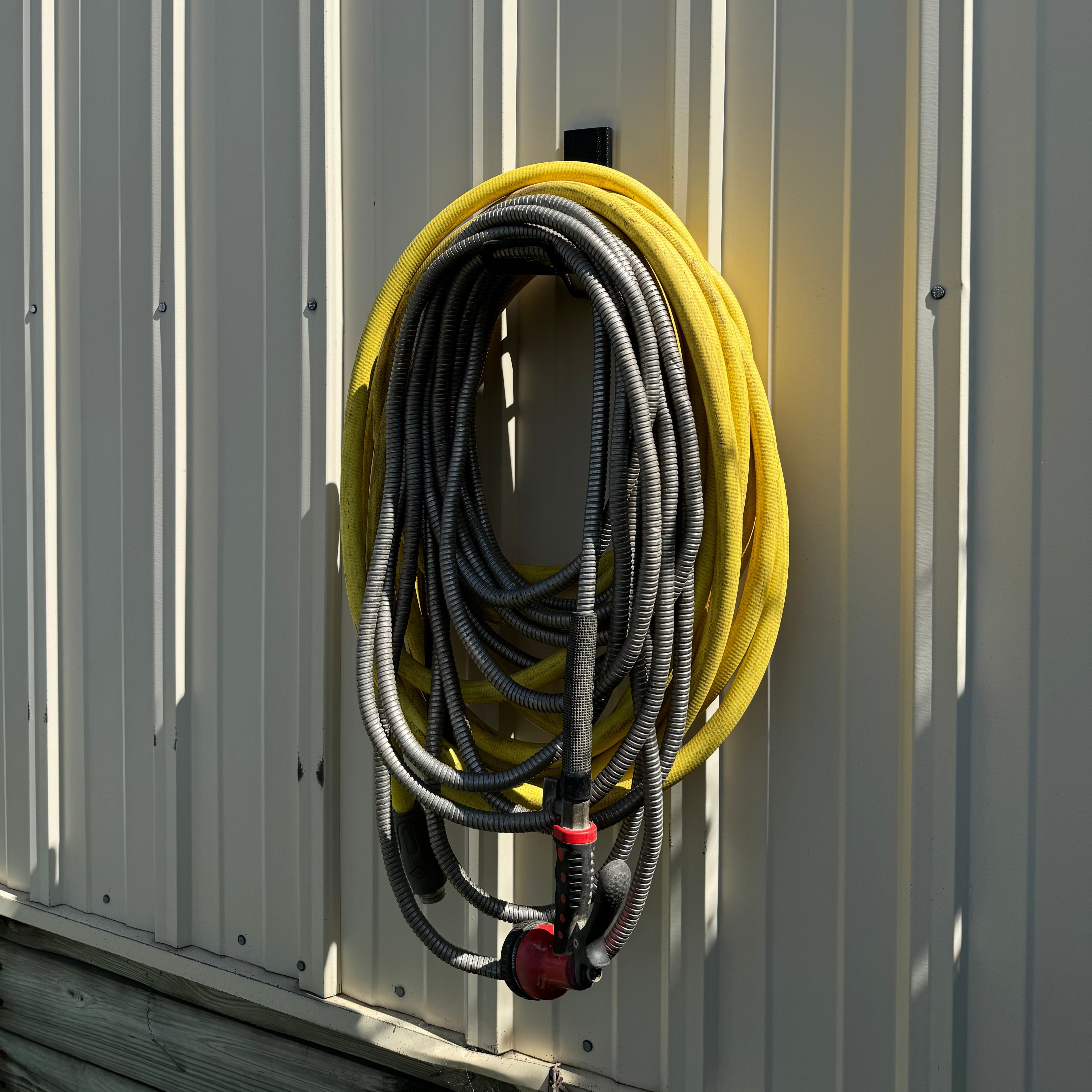 Red magnetic hook from Gator Magnetics secures coiled yellow and black hoses on a vertical steel wall panel outside a pole barn, demonstrating grinder hook up capability for organized outdoor storage.