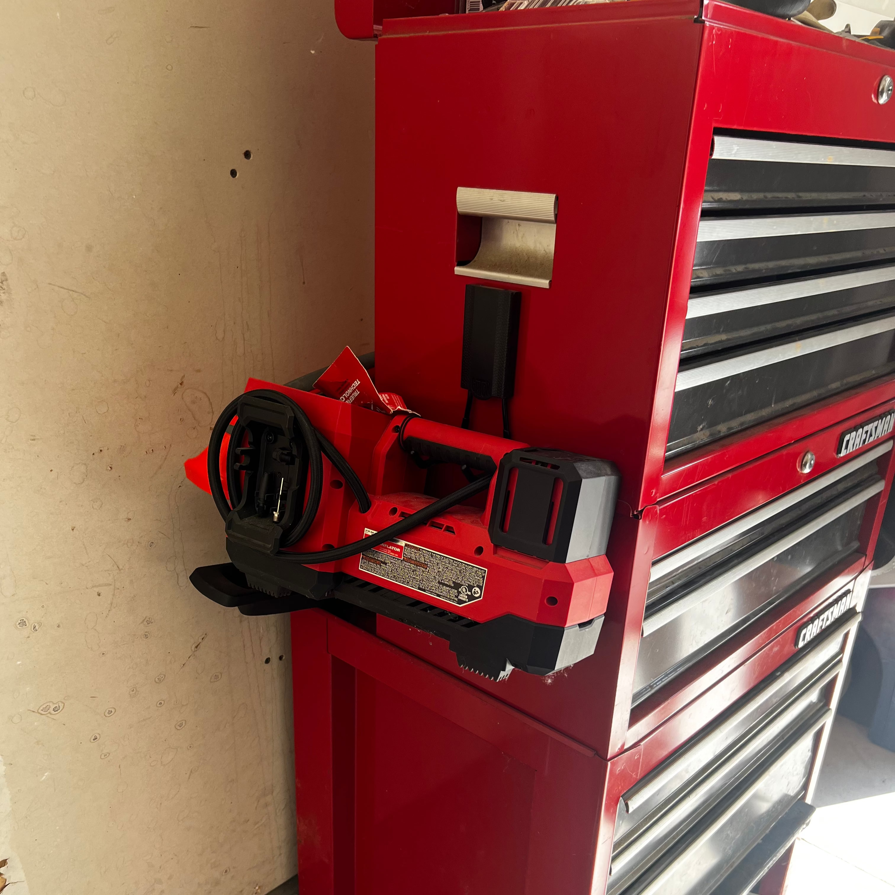 A red power tool battery charger is hung by a Gator Magnetics magnetic hook on the steel side panel of a red Craftsman tool chest, demonstrating practical shop organizer ideas.