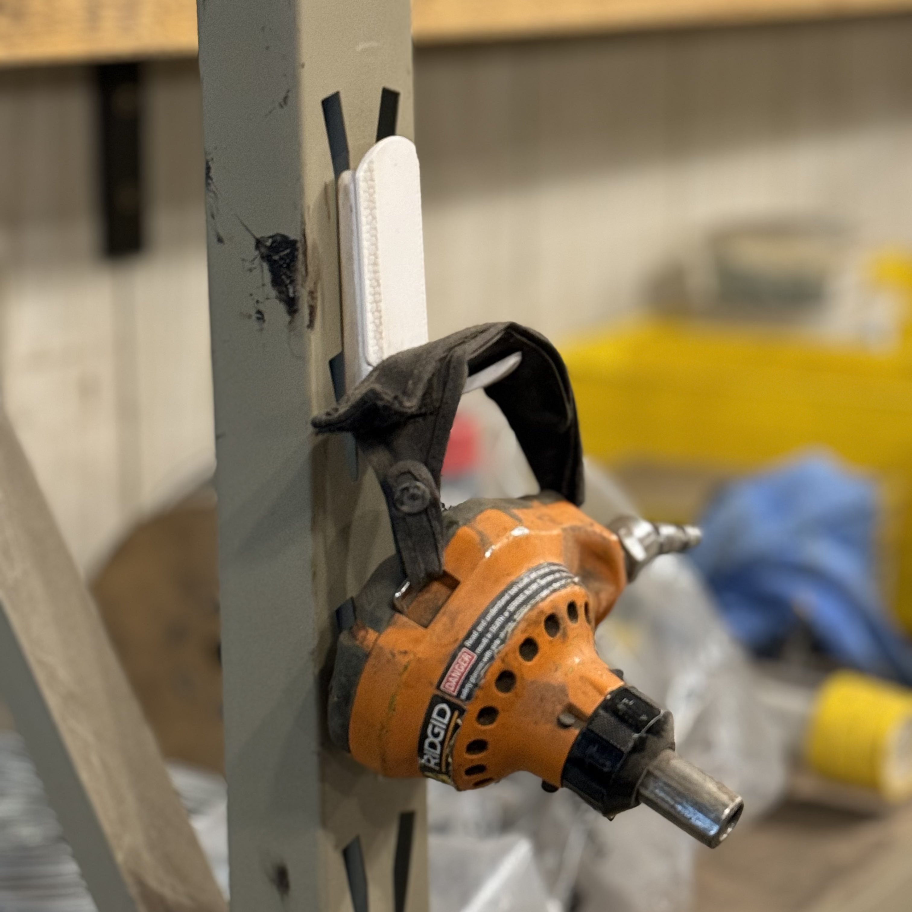 A black and orange Ridgid hand-held drain auger is supported by a white Gator Magnetics magnetic hook attached to a painted steel pole in a workshop or garage setting, demonstrating the magnetic power tool holder's secure storage capability.